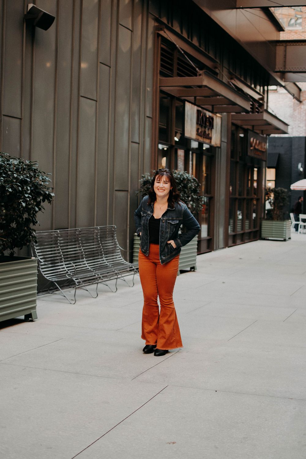 Street style photo showing retro-inspired outfit near modern storefront with metal bench.