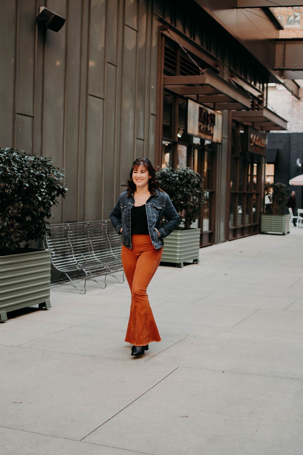 Urban fashion shot with retro 70s style outfit near modern storefront and planters.