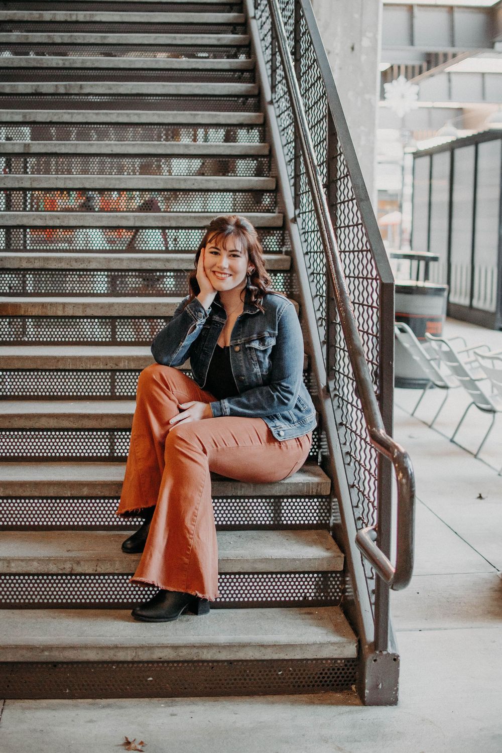 A person in denim and orange pants sits casually on industrial metal stairs in an urban setting.