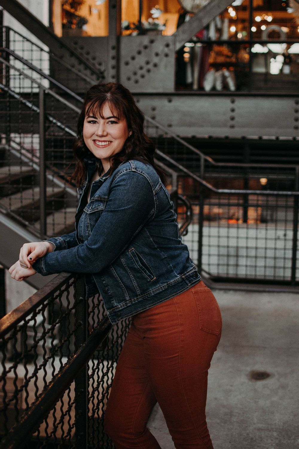 A person in casual attire leans against an industrial railing with warm lighting in the background.