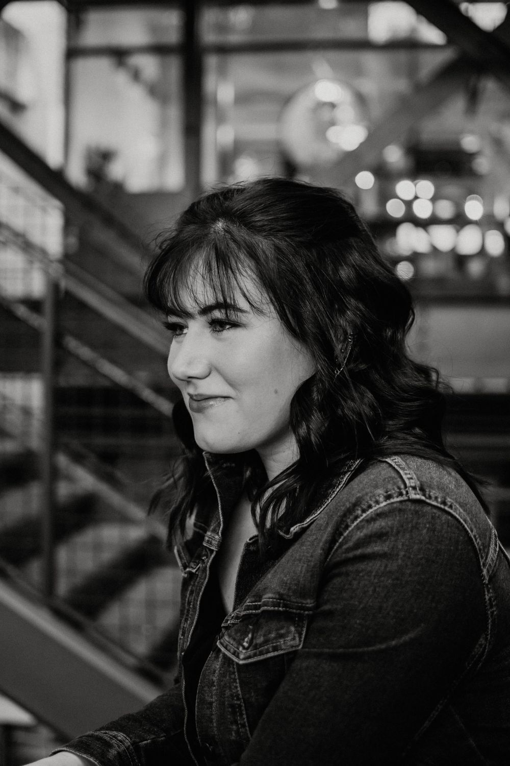 A black and white portrait of a person in denim against an industrial staircase backdrop.