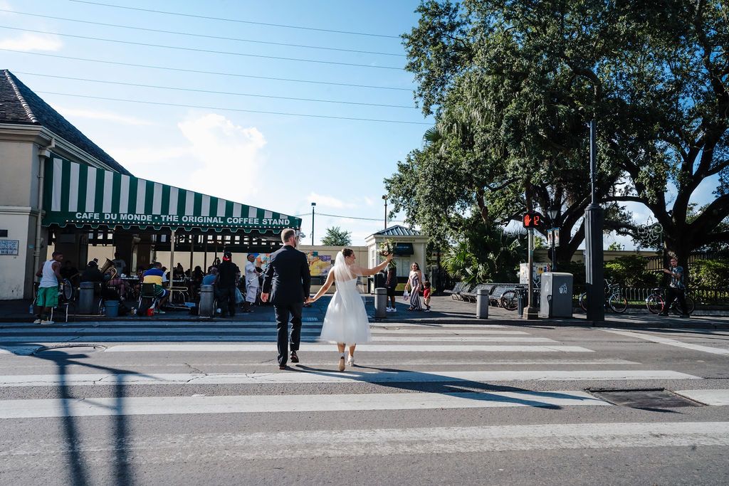 A bride and groom hold hands while walking towards Cafe du Monde in the French Quarter.