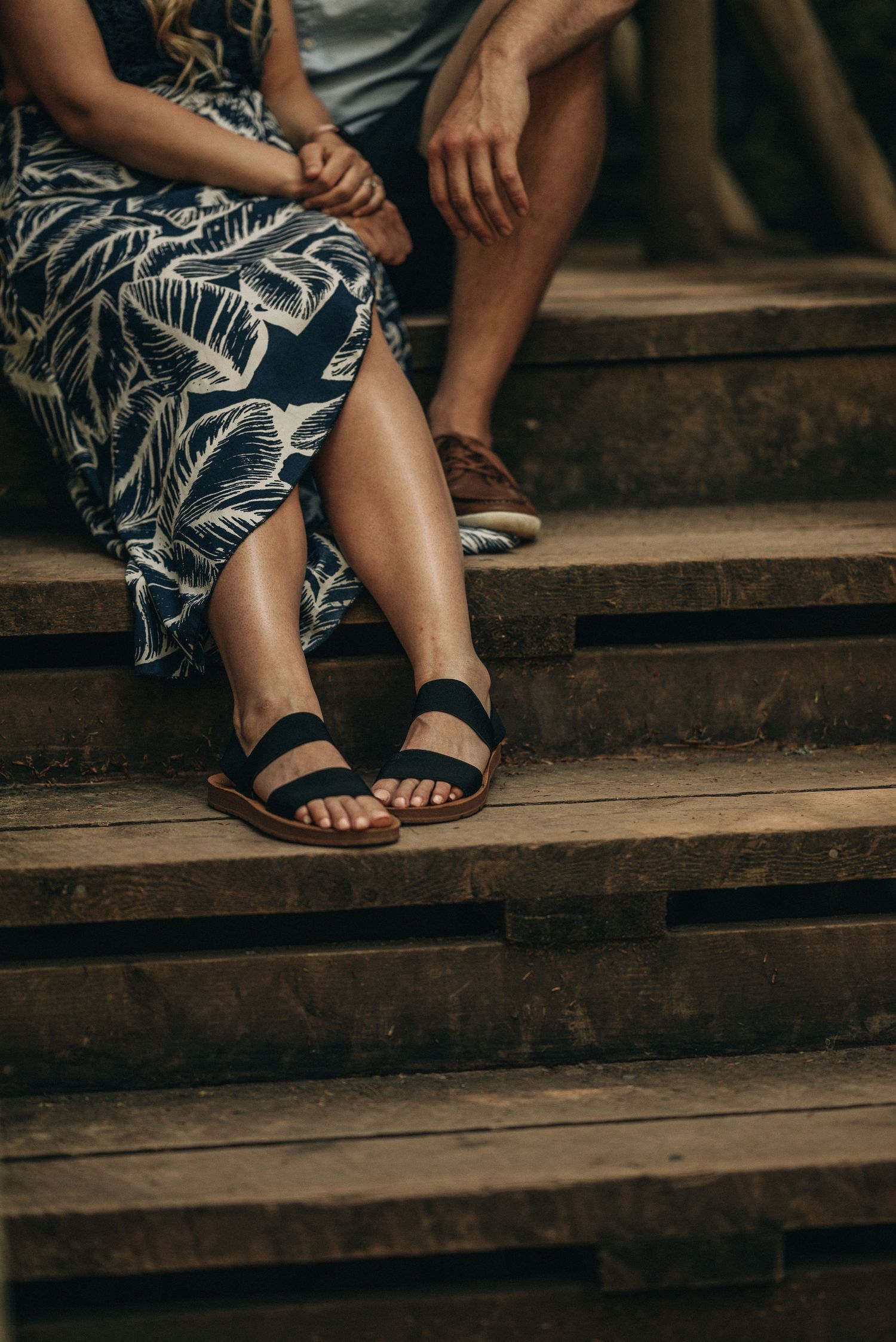 Close-up of legs wearing sandals on wooden stairs with a floral dress pattern.