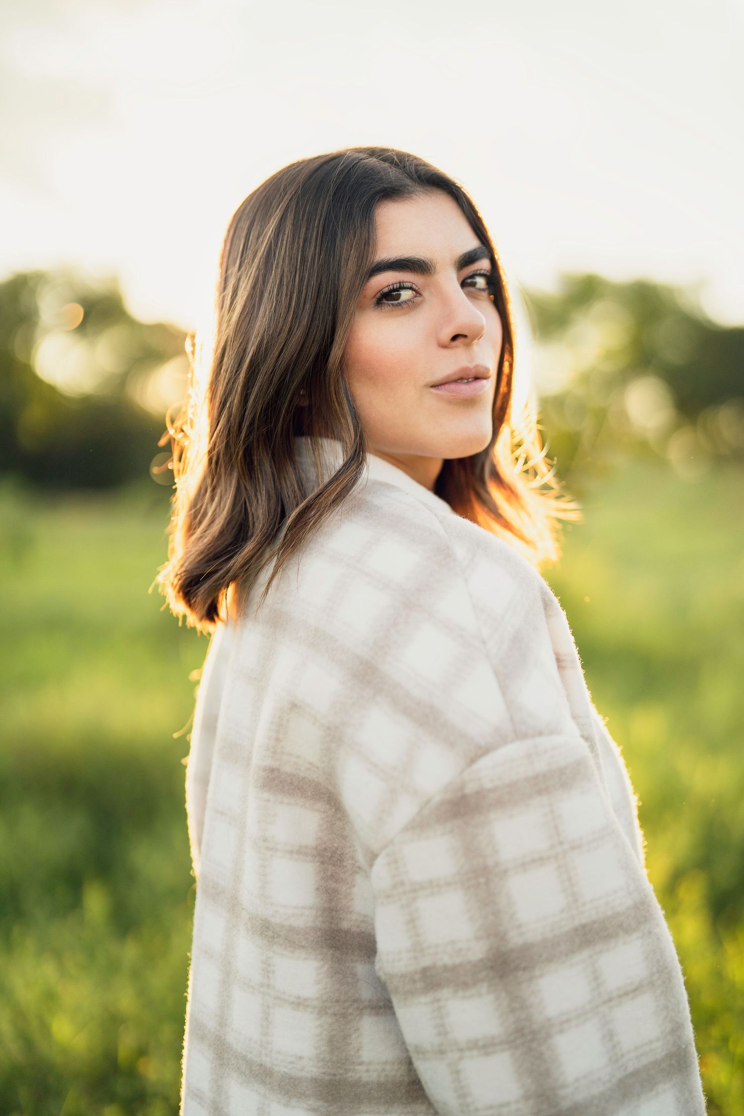 Person wrapped in a soft white blanket photographed in golden sunlight against a green field.