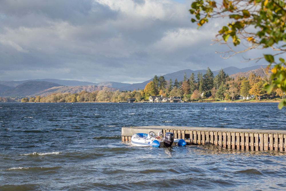 Wooden dock extending into a lake with mountains and fall foliage in the background.
