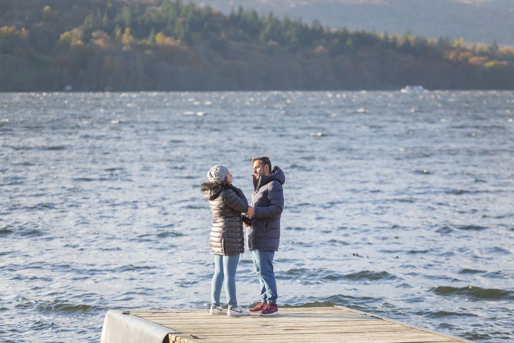 Two people standing on a dock overlooking a scenic lake with mountains in the background.