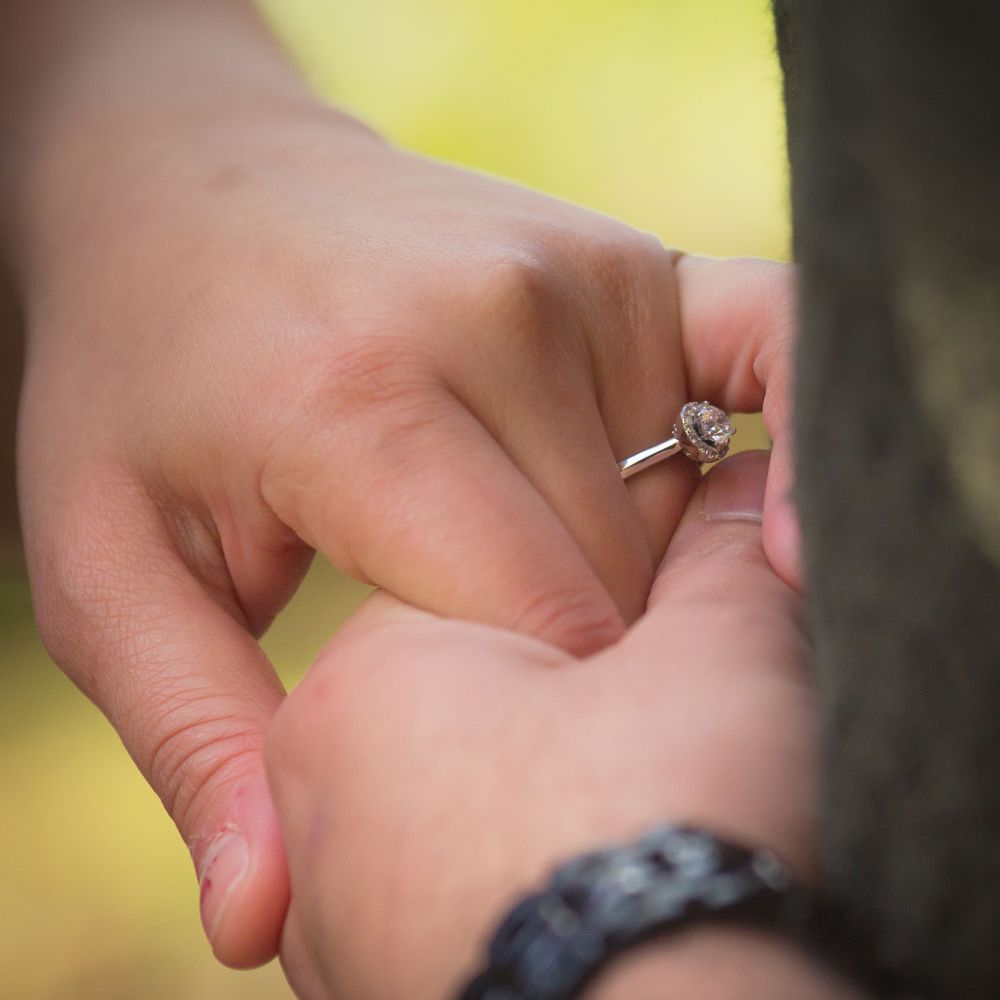 Close-up shot of hands with an engagement ring being placed on a finger.
