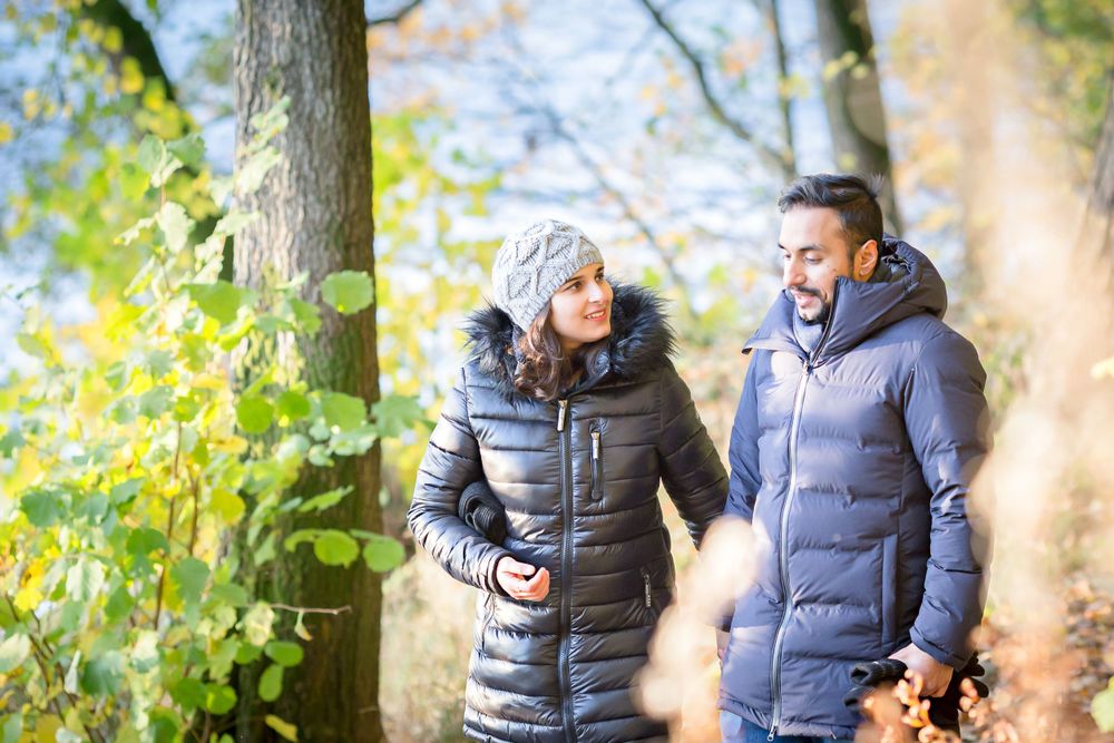 A couple in winter coats walks together on an autumn path surrounded by colorful trees.