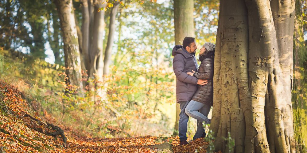 A couple shares an intimate moment among fall trees on a wooded hillside path.