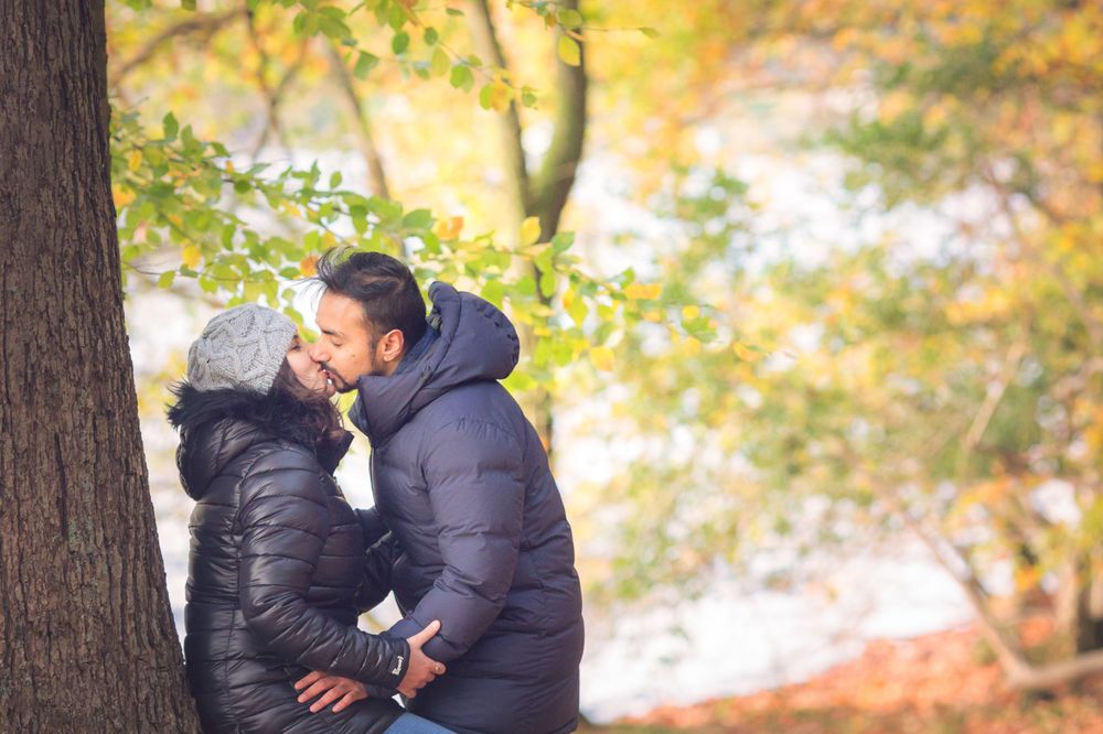 Two people in warm winter coats share a tender moment in a sunlit autumn forest.
