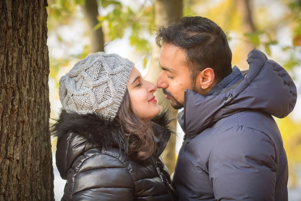 A romantic autumn moment between a couple wearing winter coats sharing an intimate moment near a tree.