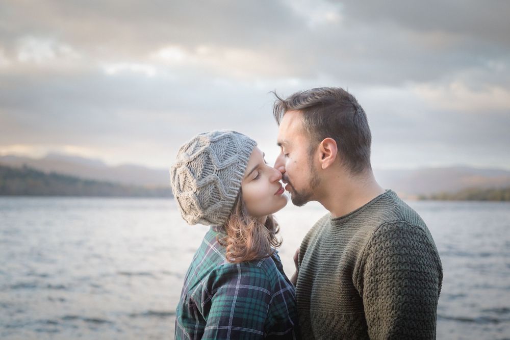 An intimate lakeside moment between a couple with mountains and moody skies in the background.
