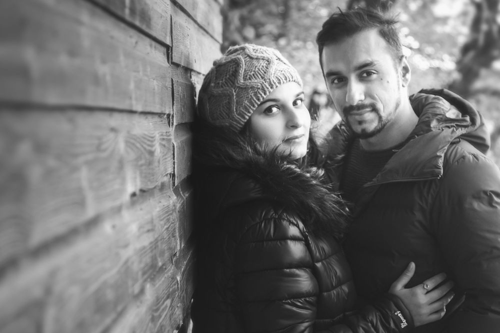 A black and white portrait of a couple in winter clothing against a textured wall.