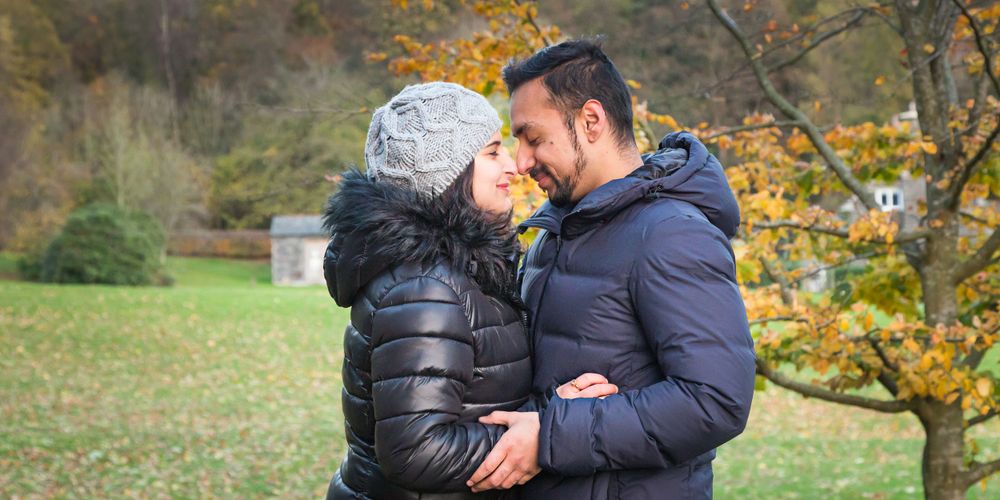 Intimate moment between couple in winter coats against autumn scenery.