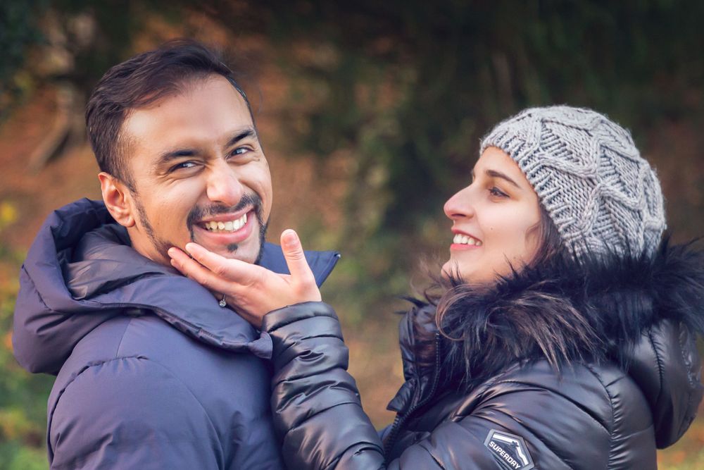 Playful winter engagement photo with couple laughing in outdoor autumn setting.