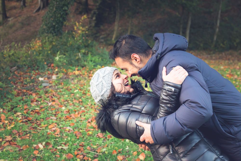 A romantic autumn moment captured between two people in warm jackets sharing a playful embrace among fallen leaves.