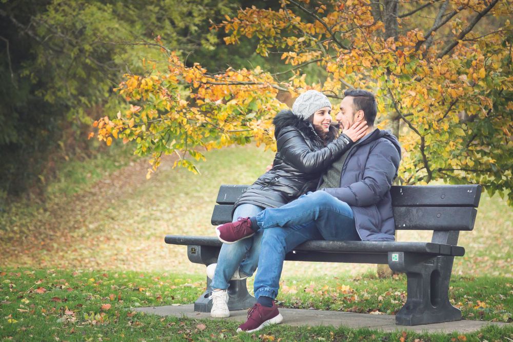 A couple sharing an intimate moment on a park bench surrounded by vibrant autumn foliage.