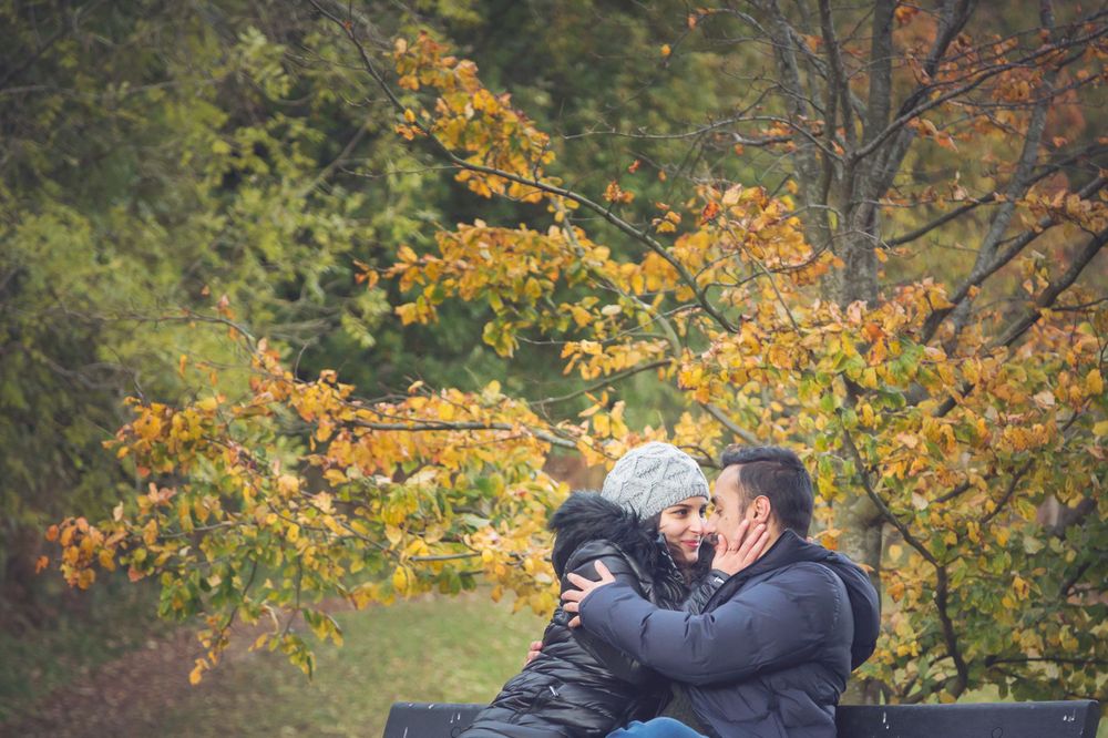 A tender moment shared on a wooden bench with golden fall leaves in the background.
