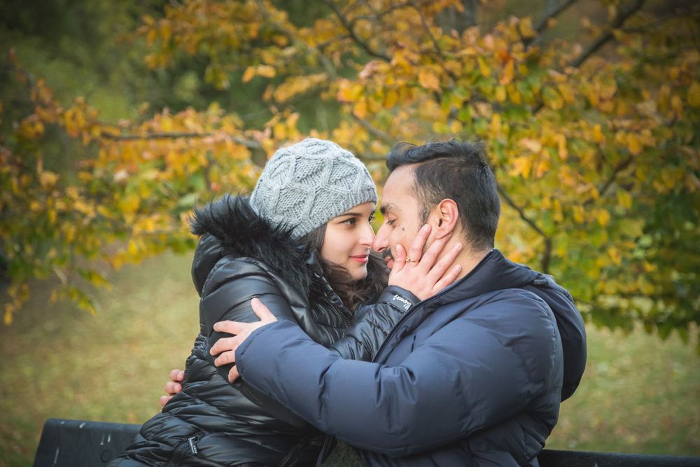 A sweet winter embrace captured outdoors with autumn trees in the background.