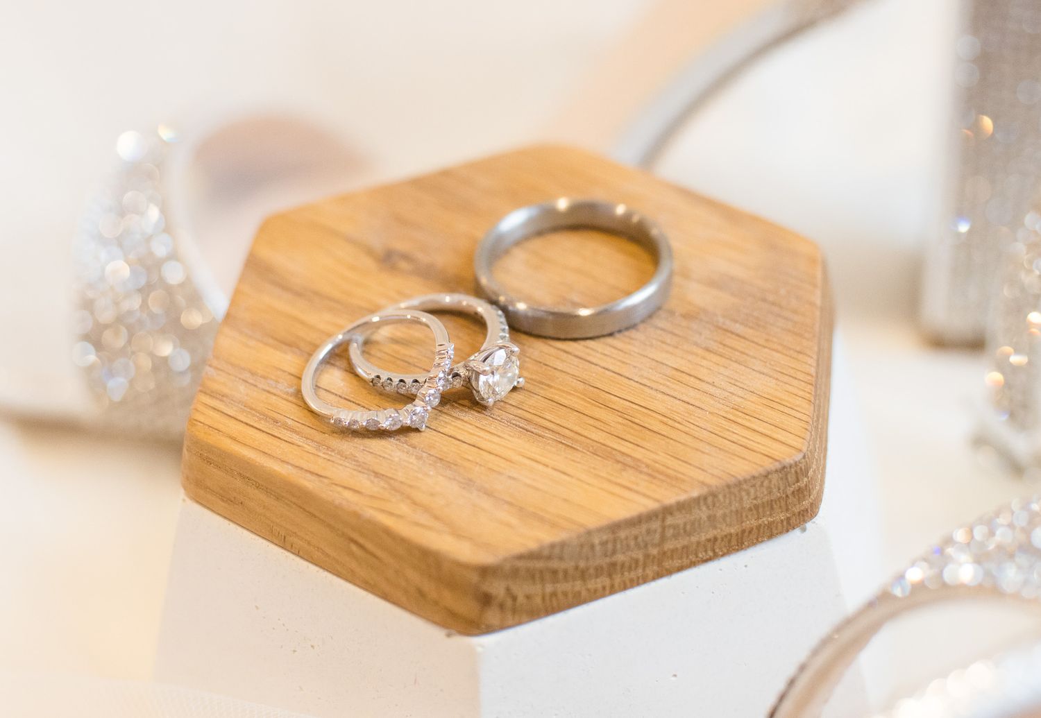 Wedding rings displayed on wooden hexagon shaped holders against a light neutral background.