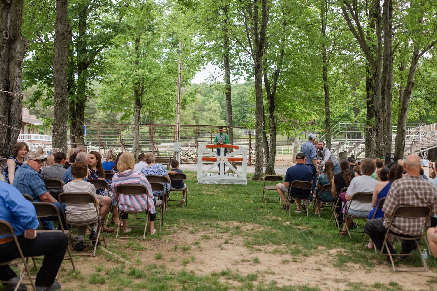 Guests seated on chairs at an outdoor wedding ceremony in a wooded setting.
