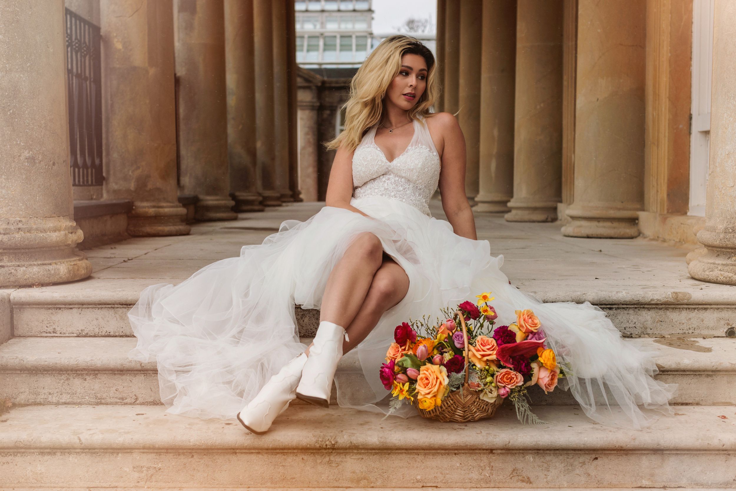 A bride sat on a step wearing a white wedding dress with flowers next to them looking off the side
