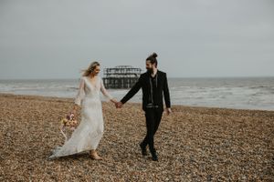 A couple in their wedding clothing on Brighton Beach with the West Pier in the background