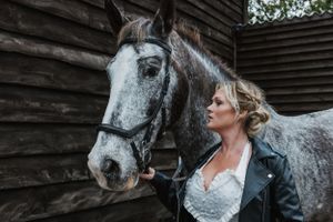 a female blonde model wearing a wedding dress and holding onto Thomas a black and grey horse