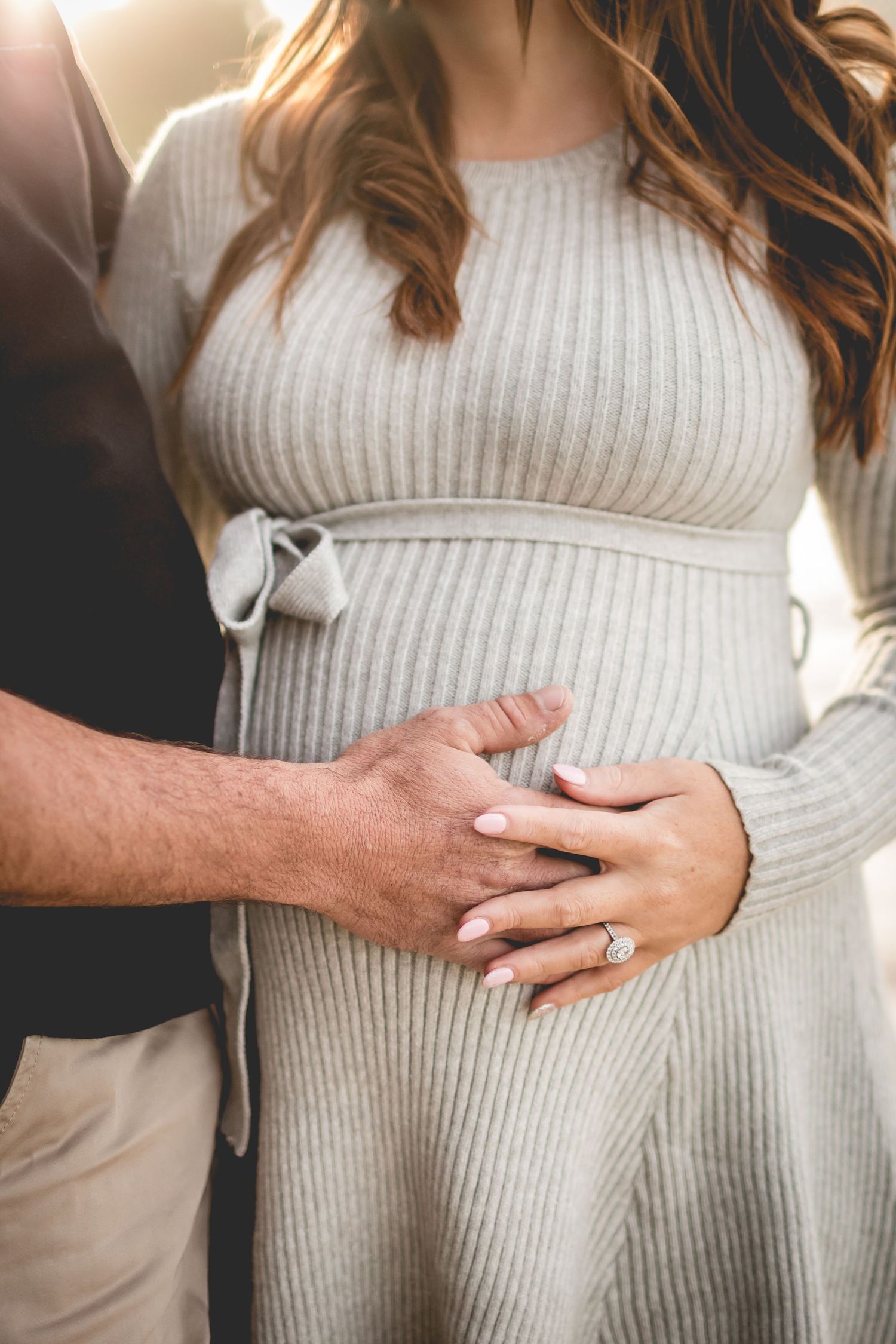 Close up of hands tenderly resting on gray sweater dress with bow detail.