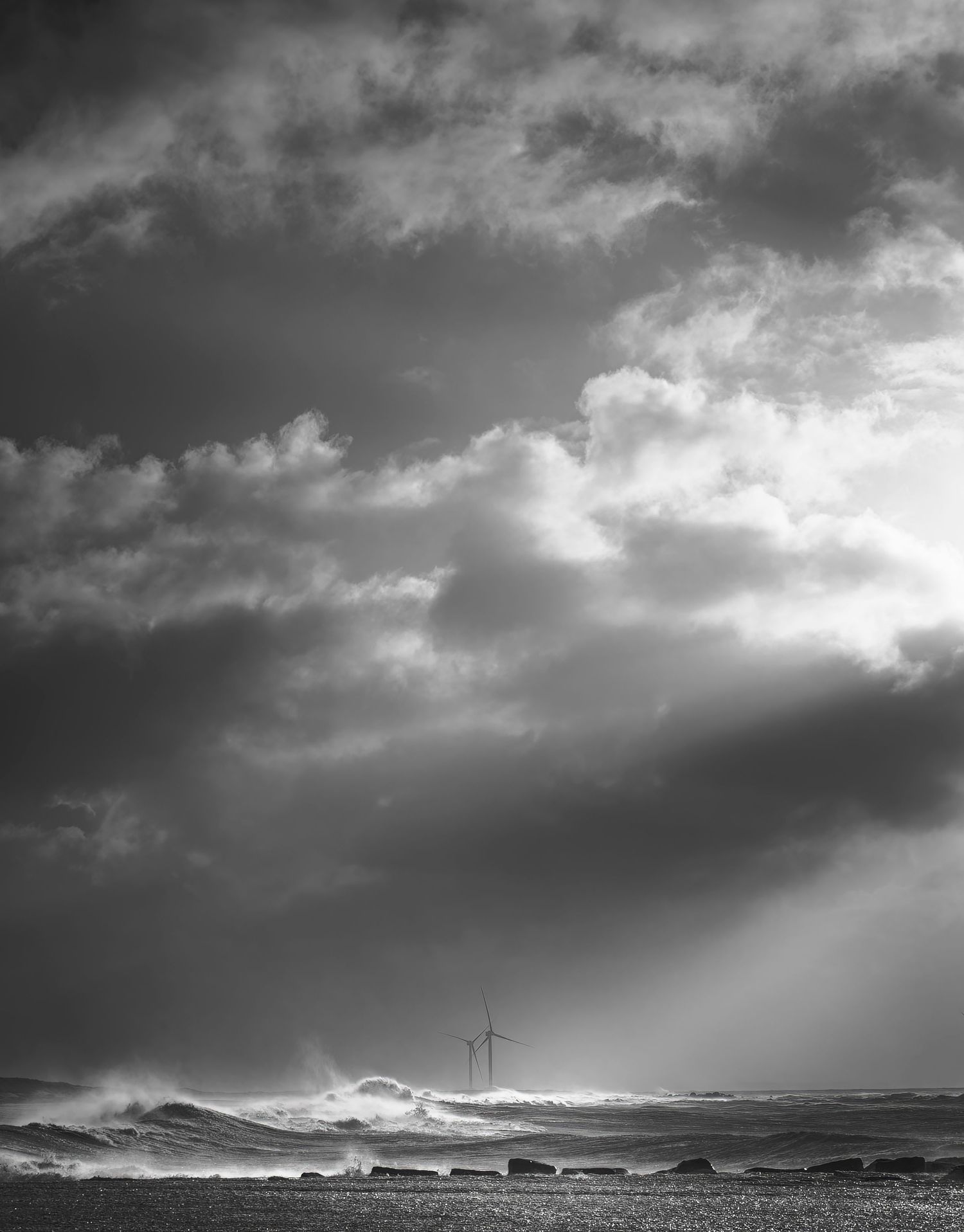 Dramatic black and white cloudscape over a wind turbines dotting the horizon.