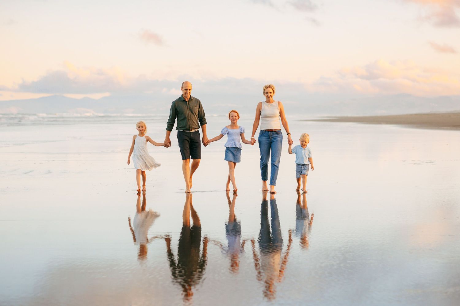 Family of 5 all holding hands walking, with reflections on the wet sand at the beach at sunset in Christchurch NZ