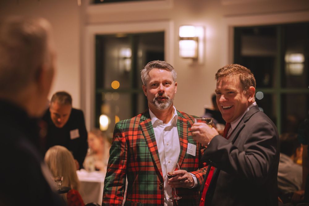 Attendees at a holiday party converse while enjoying drinks and wearing festive attire.