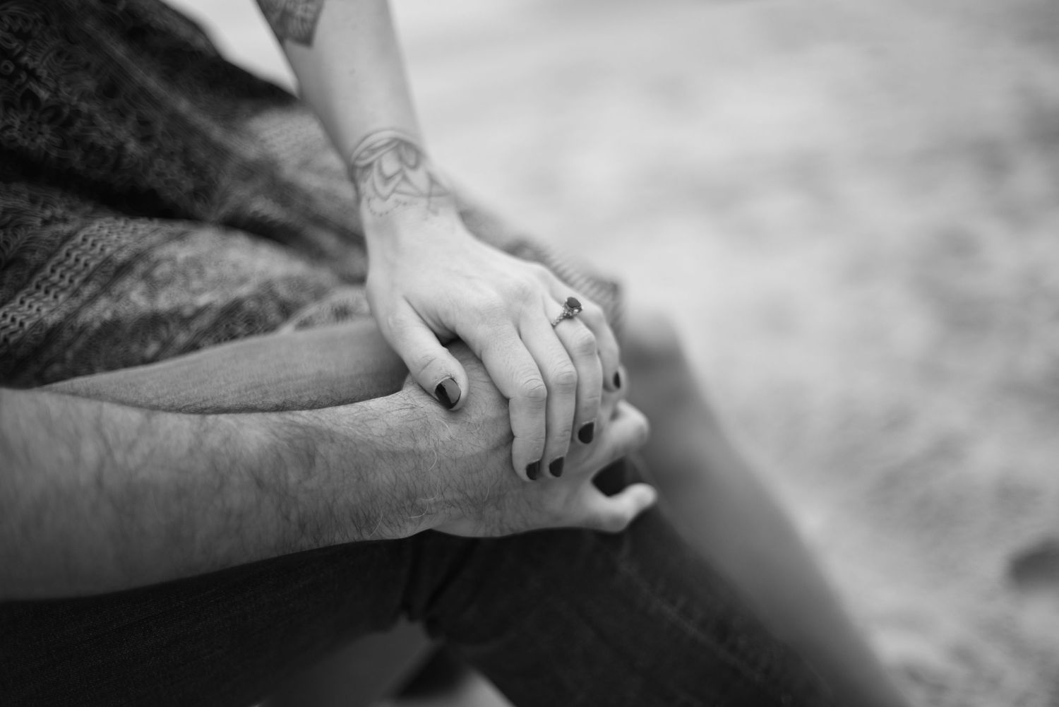 A close-up of intertwined hands with an engagement ring on the beach.