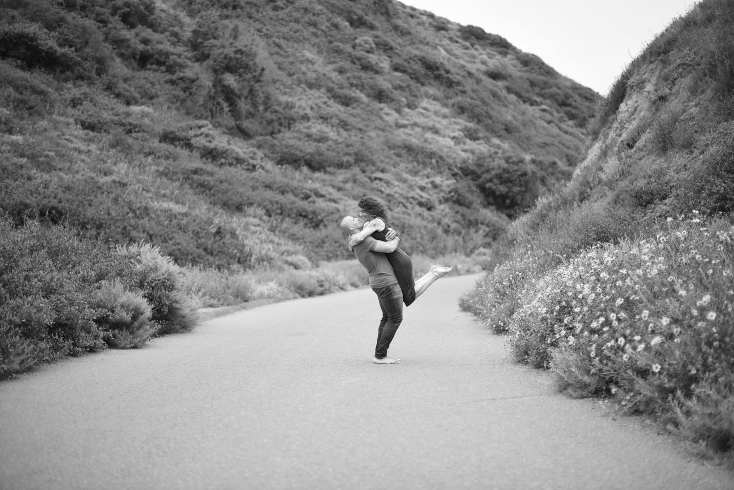 Joyful black and white photo of person leaping on path between hillsides.