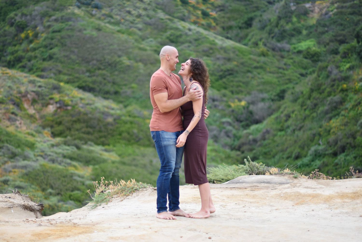 Couple sharing intimate moment on clifftop overlooking green coastal hills.