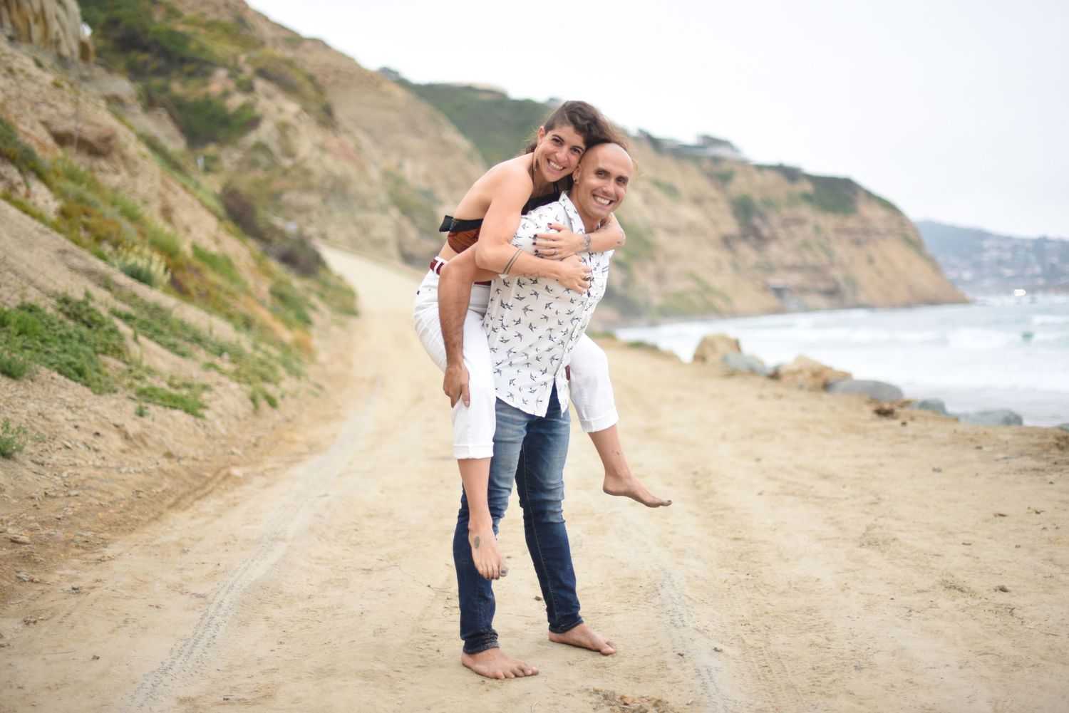 Couple sharing romantic moments on a scenic coastal cliff path with ocean views in the background.
