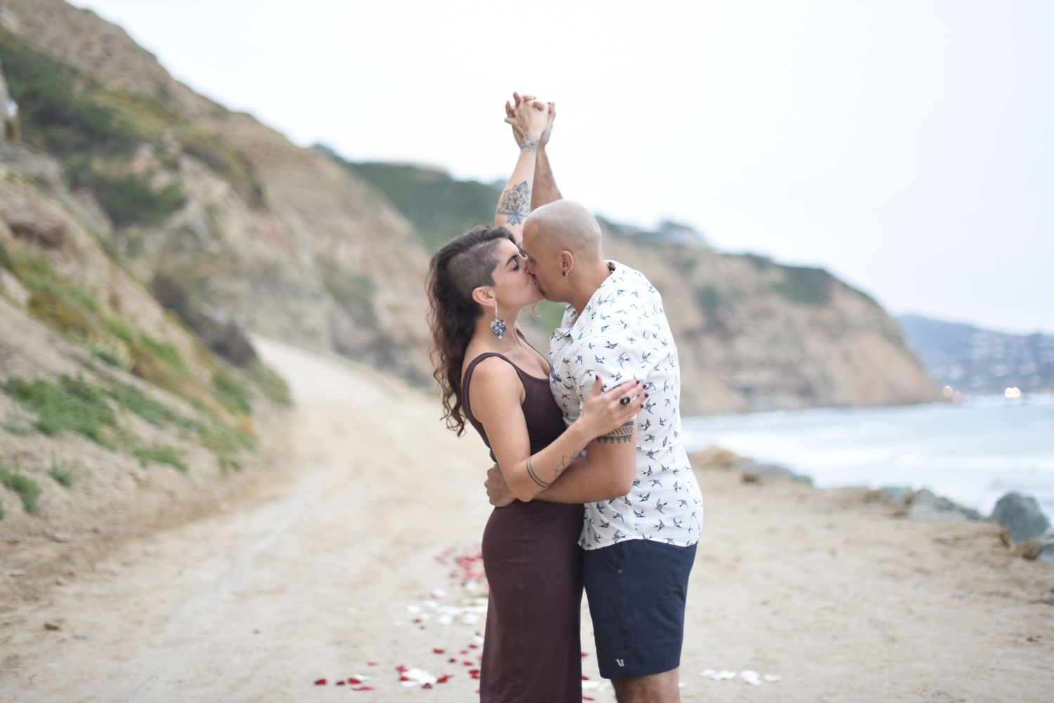 Romantic couple sharing tender moments along a coastal path with cliffs and ocean views.