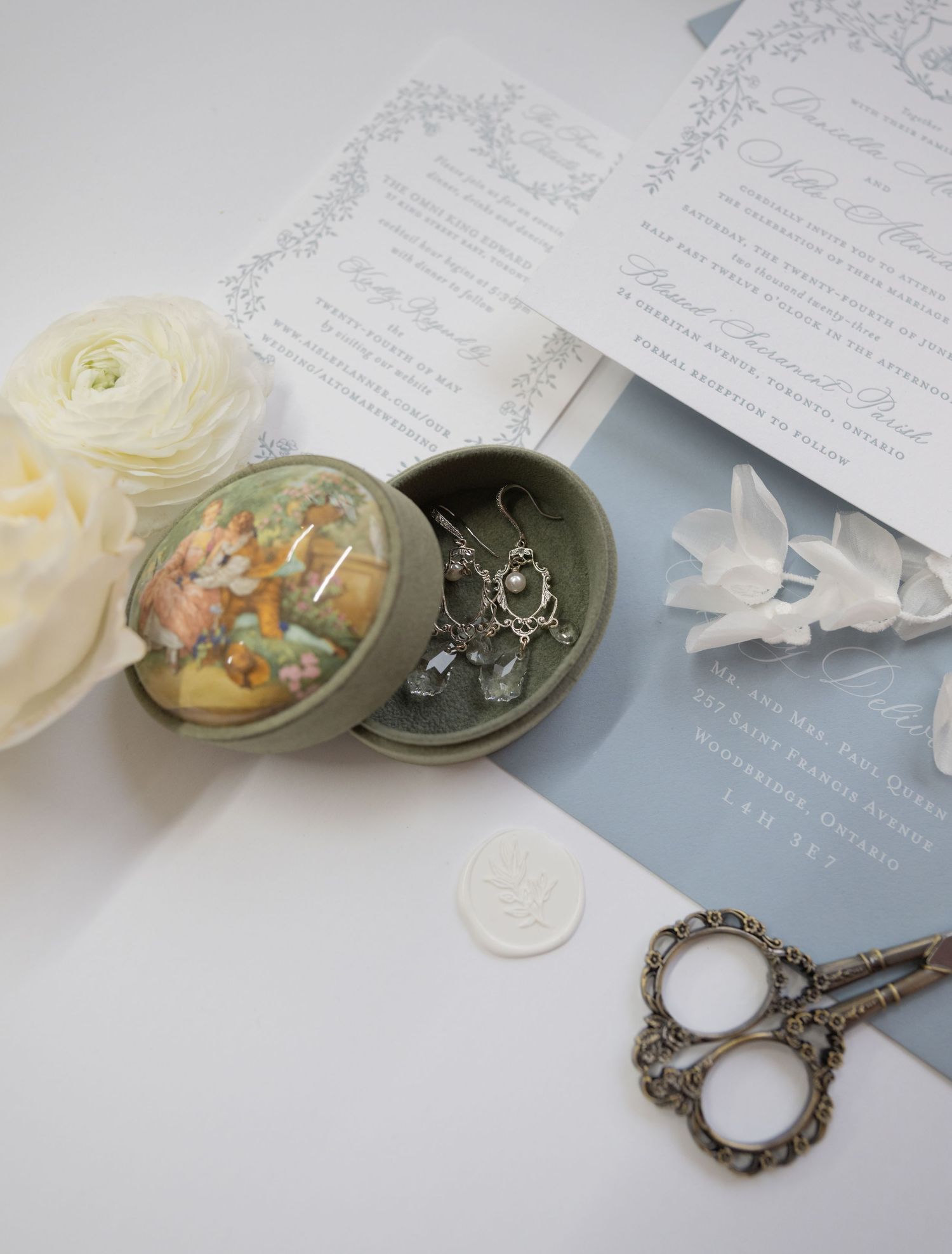 Vintage trinket box with decorative scissors and white ranunculus flowers next to wedding invitations.