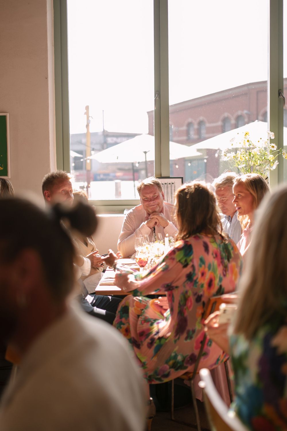 Diners enjoying a meal together in a bright restaurant with large windows overlooking city buildings.