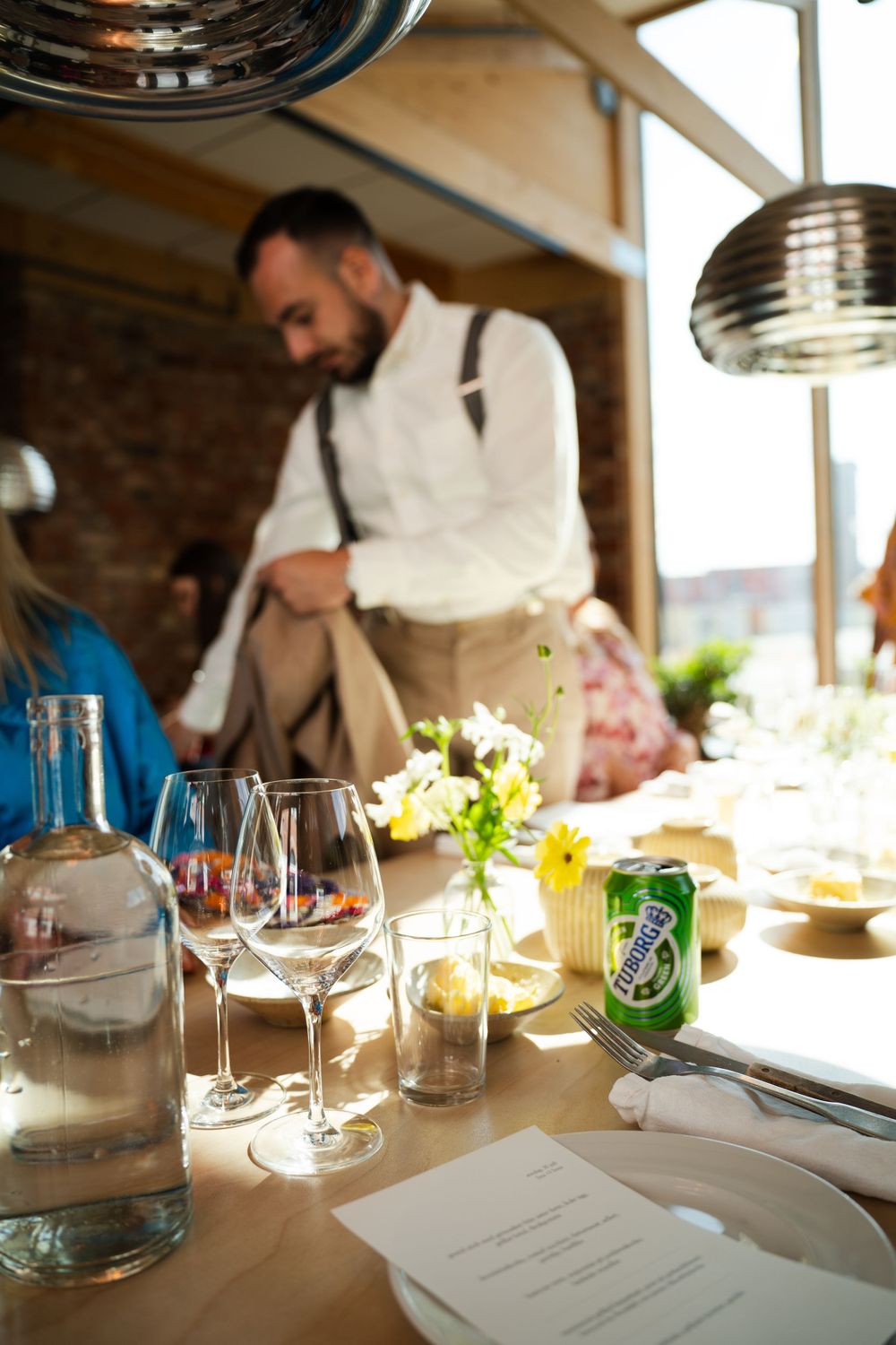 Table set for dining with wine glasses, menus and refreshments in an industrial-style space.
