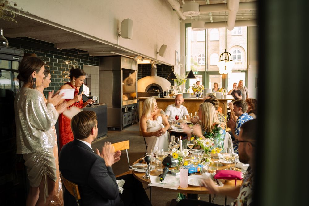 Restaurant dining scene with wood-fired pizza oven and guests gathered around tables in warm lighting.