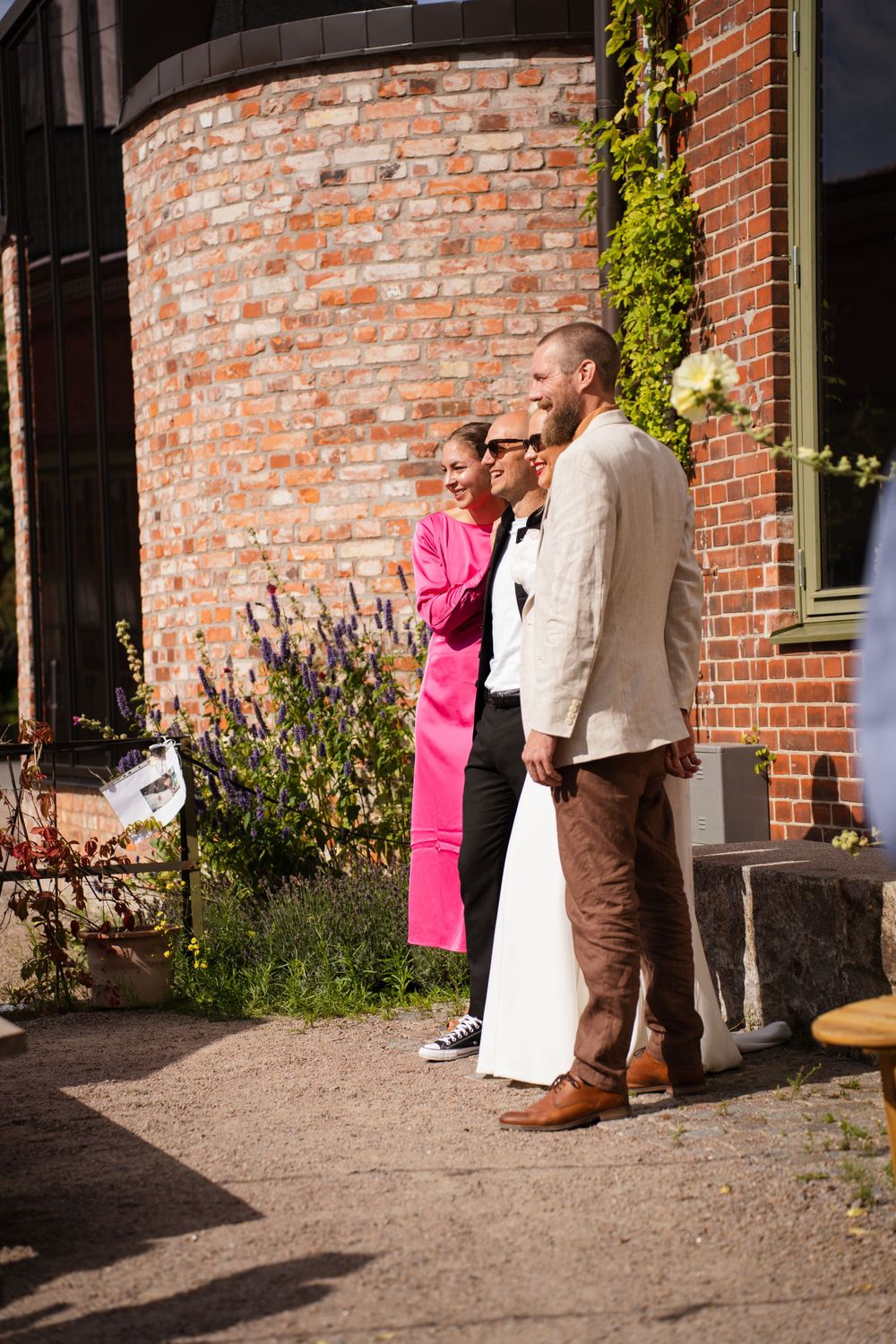 Three people in formal attire standing together against a red brick wall with climbing vines.