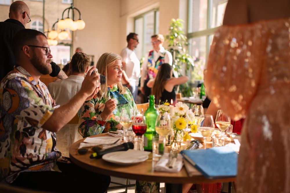 Celebratory dinner scene with guests enjoying drinks at a restaurant table.