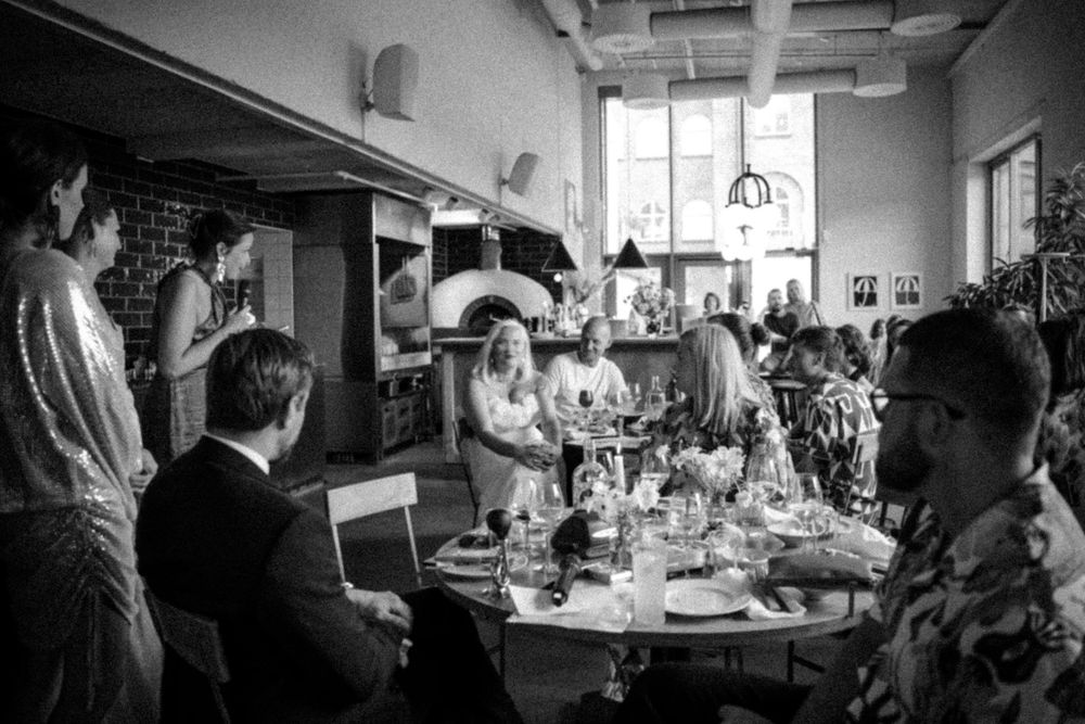 Black and white photo of diners and staff in a restaurant with brick walls and pendant lighting.