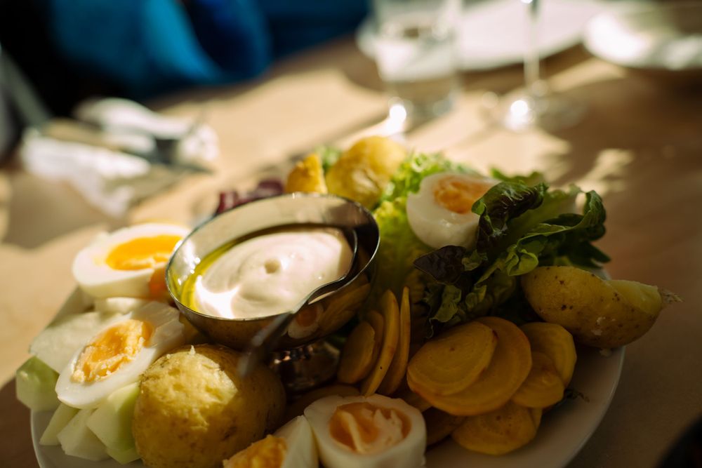 Close-up of an elegant plated dish featuring sliced eggs, greens and dipping sauce.