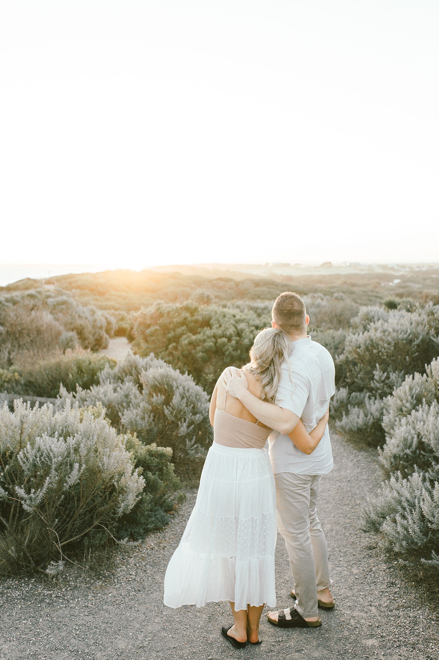 Couple embracing while watching the sunset over rolling hills covered in sage brush.