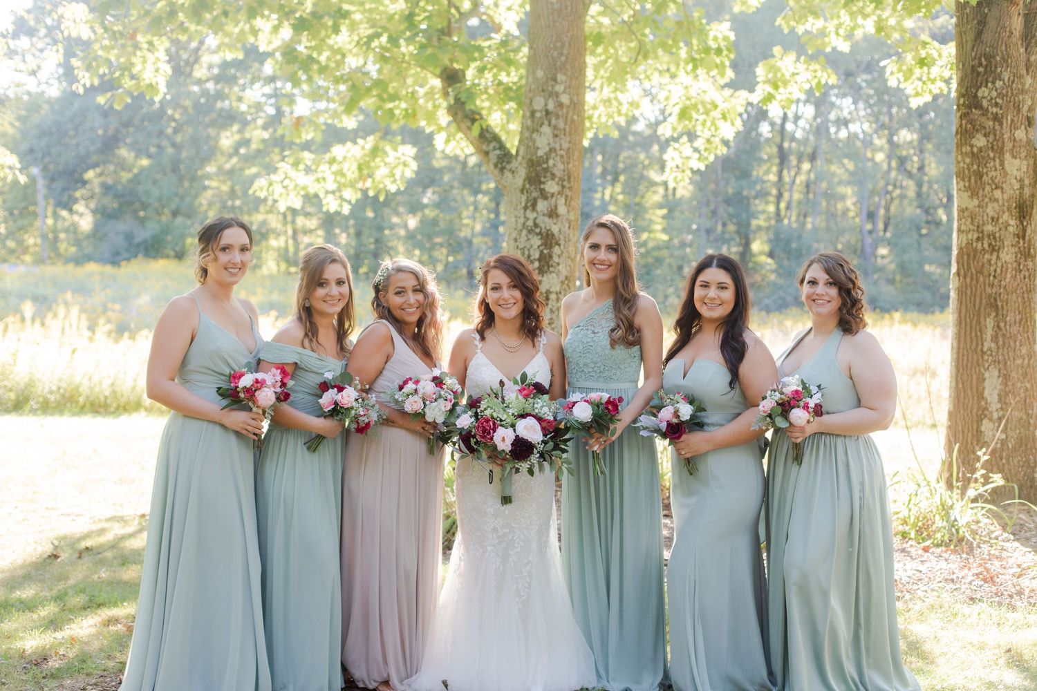 Bridesmaids in sage green dresses pose together outdoors for wedding photos.