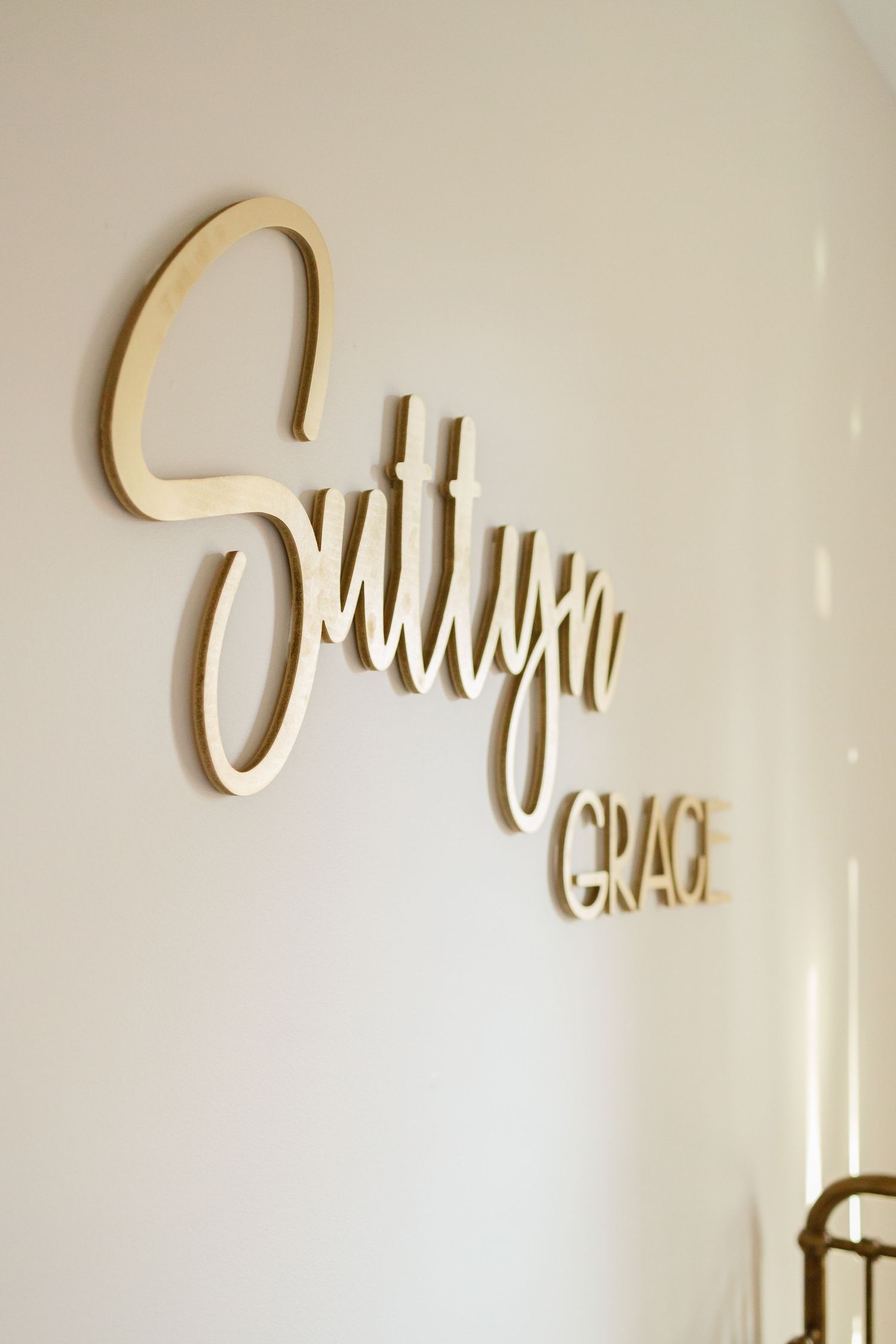 Wooden script wall art mounted on a cream colored wall displays decorative text.
