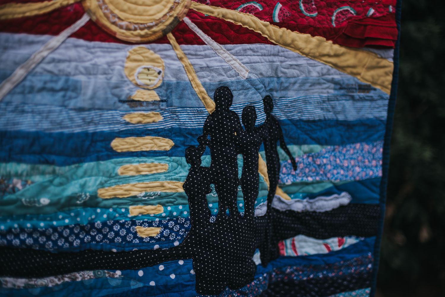 Applique of a group of children in the water on a memory quilt made from their clothing.