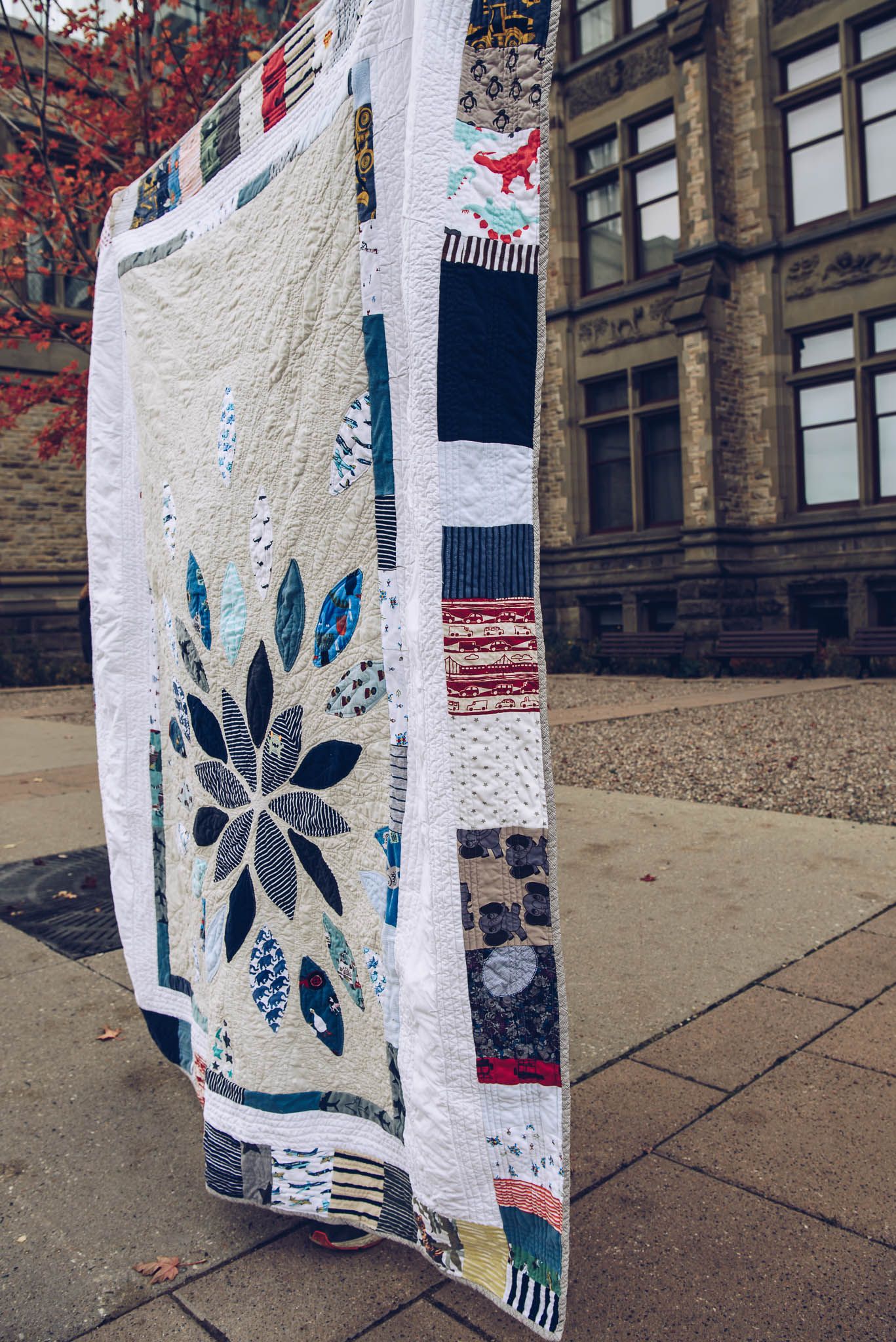 Starburst memory quilt being held up in front of a building.